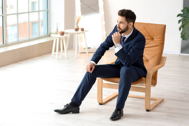 Стильный молодой человек сидит в кресле в помещении
 - Фото, изображение