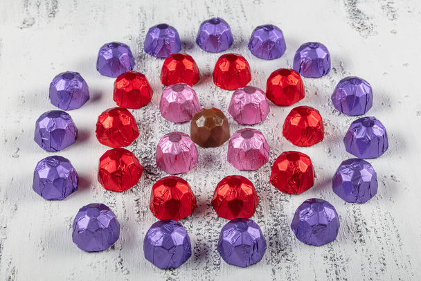Foil covered gift chocolates. Chocolate truffle candies arranged in rows on white wooden background. - Foto, immagini