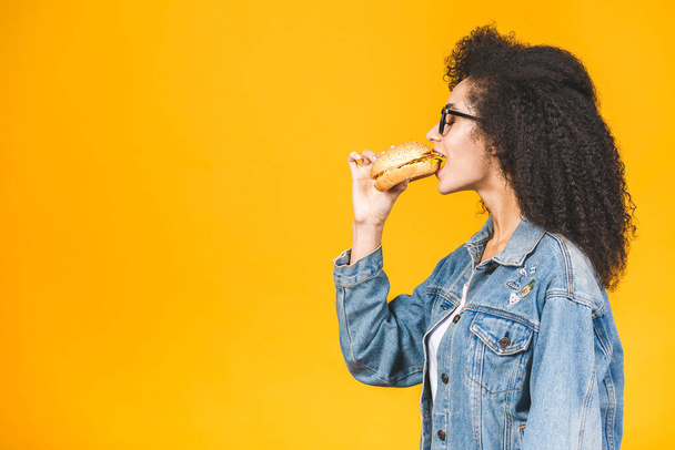 Афроамериканская черная молодая женщина ест гамбургер изолирован на желтом фоне
. - Фото, изображение