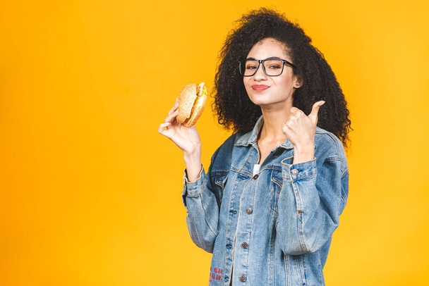 Afroamerikanisch schwarze junge Frau isst Hamburger isoliert auf gelbem Hintergrund. - Foto, Bild