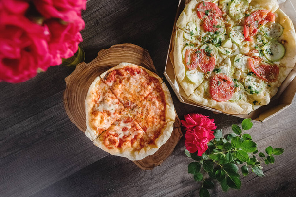 Appetizing pizza on a wooden table, on a tray, with a bouquet of roses. The concept of food and pastime - Φωτογραφία, εικόνα