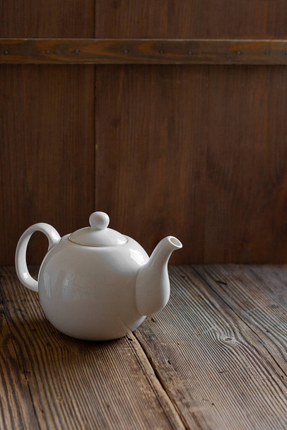 White ceramic mockup teapot for hot tea on empty old wooden table near wall made of brown timber planks. Vertical banner with copy space. Rustic style. - Foto, afbeelding