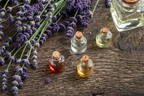 Several bottles of essential oil with blooming lavender twigs - Fotó, kép