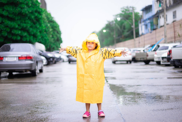 pieni aasialainen tyttö yllään sadetakki seisoo kadulla - Valokuva, kuva