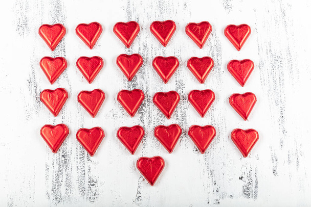 Herzförmige Schokoladenbonbons in roter, bunter Folie zum Valentinstag. Valentine Bild auf weißem Holzhintergrund. - Foto, Bild