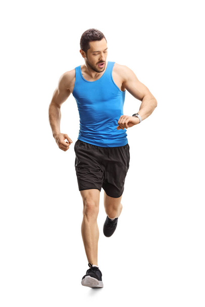 Full length portrait of a man in sportswear running towards the camera and looking at his smartwatch isolated on white background - Photo, Image