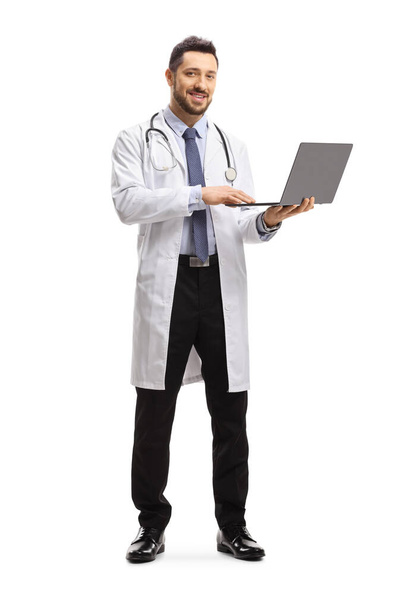 Full length portrait of a male doctor standing and using a laptop computer isolated on white background  - Foto, imagen