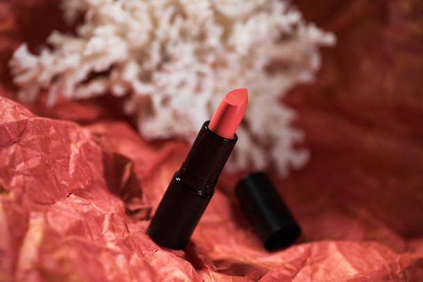 Rouge à lèvres sur fond rouge avec image floue de corail. - Photo, image