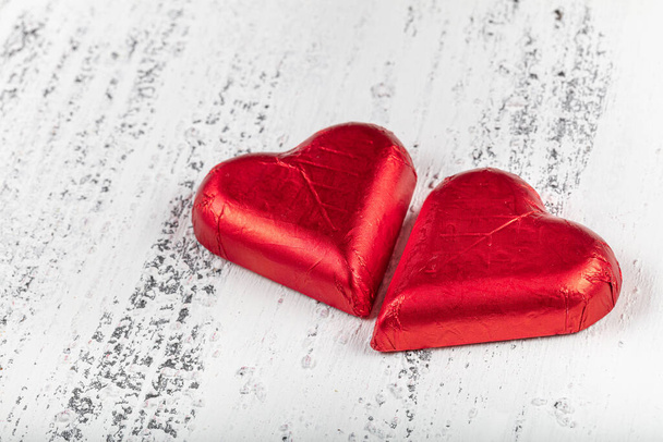 Čokoládové bonbóny ve tvaru srdce zabalené v červené barevné fólii na Valentýna. Valentýn obrázek na bílém dřevěném pozadí. - Fotografie, Obrázek