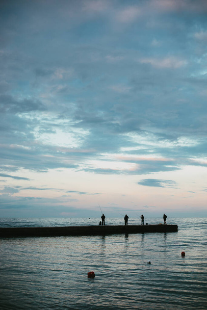 Vissers vangen vis op de pier tegen de achtergrond van de zee en de lucht - Foto, afbeelding