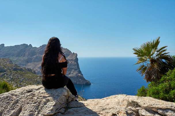 Latijns meisje, met lang golvend brunette haar, poseren voor, portret, op een lentedag met bril, zittend op de klif van Cap de Formentor Mallorca, Balearen, Spanje, - Foto, afbeelding