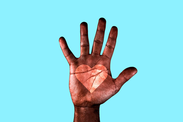 Palma aberta de um homem afro-americano com um coração desenhado pedindo o fim do racismo. Mão preta isolada em um fundo azul
. - Foto, Imagem