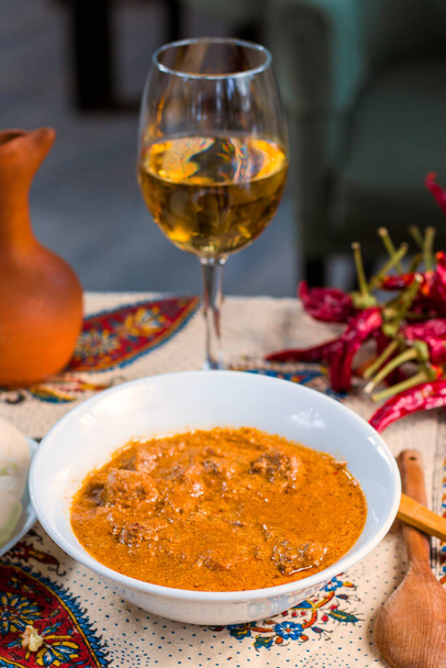 Γεωργιανή παραδοσιακή σούπα Kharcho ή καρύδια souse με μοσχαρίσιο γεύμα, ξηρό κόκκινο πιπέρι, ντομάτες και άλλα συστατικά. Με κρασί και ξύλινη κουτάλα. Τιφλίδα, Γεωργία. - Φωτογραφία, εικόνα