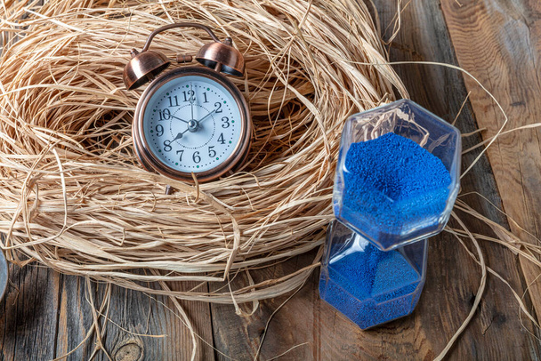 Reloj de arena azul, despertador y escamas con oro en suelo de madera. Concepto de tiempo
. - Foto, Imagen