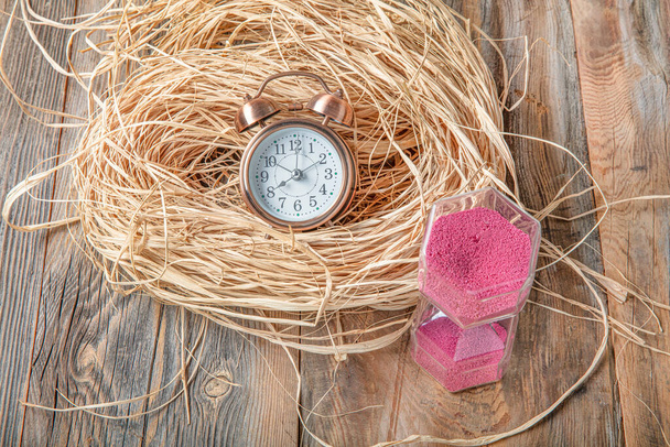 木製の床に藁にピンクの砂時計と目覚まし時計。時間の概念 - 写真・画像