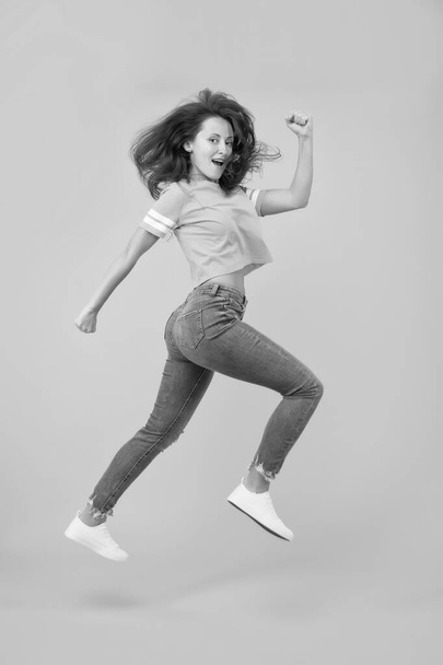 Feel inner energy. Energetic woman running or jumping. Skinny jeans suits her. Sexy girl yellow background. Sensual girl in casual style. Pretty girl with long hair. Fashion style. Beauty and make up - Foto, Bild