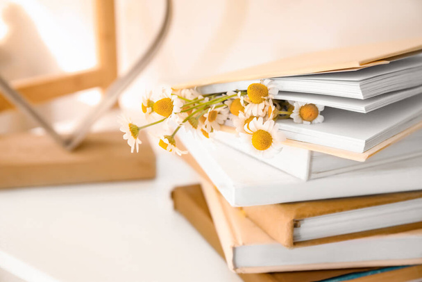 Books with beautiful chamomiles on shelf, closeup - Fotó, kép