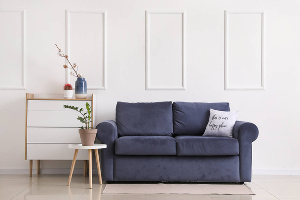 Sofá elegante, cómoda y mesa con planta de interior cerca de la pared de luz en la habitación
 - Foto, Imagen