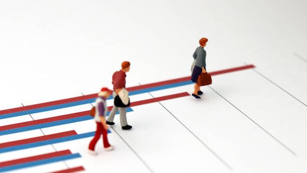 The concept of the widening income gap between people. Three miniature people walking on a bar graph. - Fotoğraf, Görsel