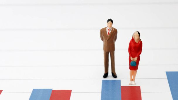 A miniature man and a miniature woman standing on top of a bar graph. - Foto, afbeelding