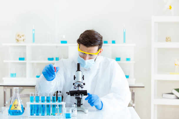 Επιστήμονες κοιτώντας μέσα από ένα μικροσκόπιο σε ένα εργαστήριο για την ανάλυση ενός δείγματος μικροοργανισμών, και τη δοκιμή χημικών αντιδράσεων για την παραγωγή εμβολίων και διαφόρων φαρμάκων. - Φωτογραφία, εικόνα