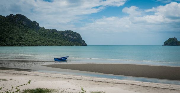 Blue fishing boat sitting in the sand at low tide with islands and blue sky in the background in Khao Lummuak - Photo, Image