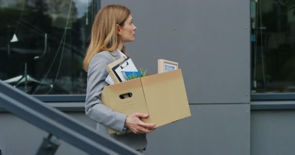 Side view on Caucasian young sad businesswoman walking down the stairs outdoor with box of stuff as leaving business center. Female office worker lost job. Unemployment rate at pandemic. Fired woman. - Footage, Video