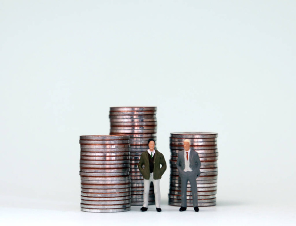 Deux hommes miniatures debout avec trois piles de pièces. Les stéréotypes sociaux sur le succès des hommes. - Photo, image