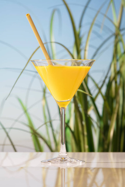 egy finom Martinis pohár narancslével és egy szívószállal az üvegasztalon. vegán étel fogalma. - Fotó, kép