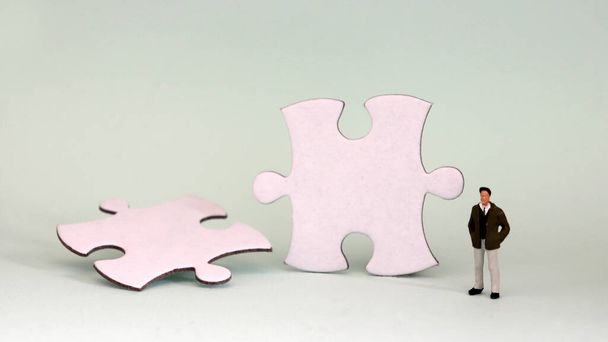 A miniature man standing with two pieces of puzzle. - Photo, Image