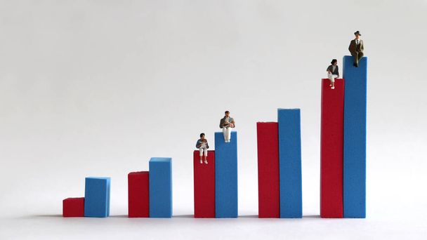 Dos mujeres en miniatura sentadas en una barra roja en un gráfico de barras y dos hombres en miniatura sentados en una barra azul. Concepto de brecha salarial
. - Foto, Imagen