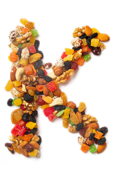 Letter K of the English alphabet from a mixture of hazelnuts, almonds, walnuts, cashews, seeds, raisins, candied fruit on a white isolated background. Food pattern made from nuts.  - Photo, Image
