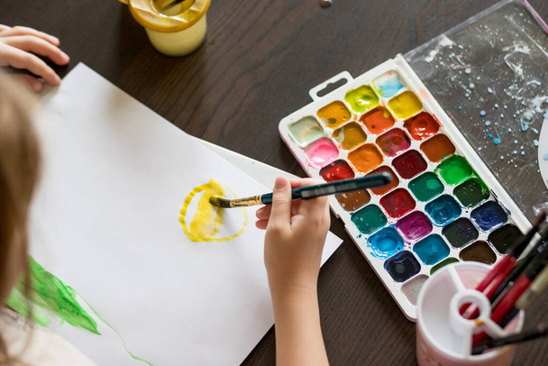 Kiválasztása színek első rajz.akvarell doboz, gyerekek kéz és ecset.Gyerek kéz festés az asztalnál a művészeti kellékeket.Tanulás festészet koncepció. Scholl lecke - Fotó, kép