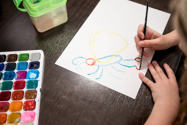 Dziecko trzyma pędzel i malowanie na białym papierze.Wybór kolorów do rysowania.Farby akwarelowe i pędzle do malowania. Kreatywność dzieci, malarstwo, wczesny rozwój. - Zdjęcie, obraz