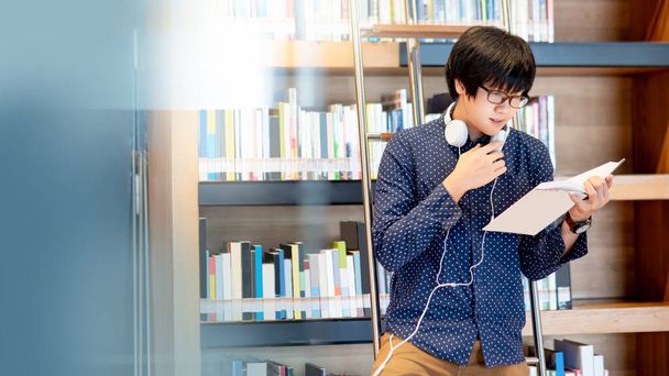 Ασιάτης φοιτητής διαβάζοντας βιβλίο από βιβλιοθήκη σε βιβλιοθήκη κολέγιο για την έρευνα της εκπαίδευσης. Συλλογή bestseller στο βιβλιοπωλείο. Υποτροφίες ή εκπαιδευτικές ευκαιρίες έννοιες - Φωτογραφία, εικόνα