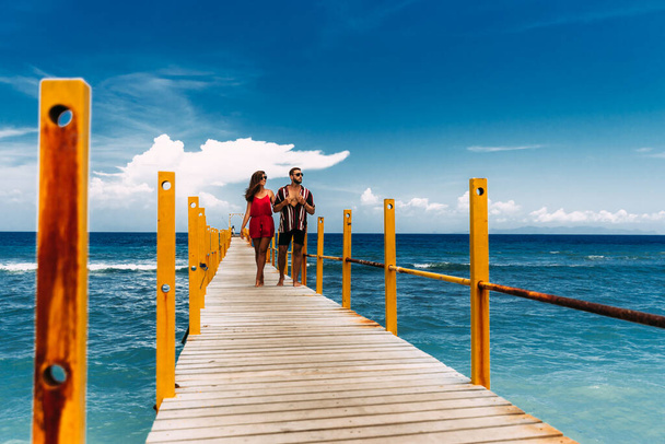 Happy couple on vacation strolling along a wooden pier above the tropical blue ocean. Beautiful couple on the coast in Indonesia. A couple in love is resting on the sea. Honeymoon trip. Copy space - Foto, Bild