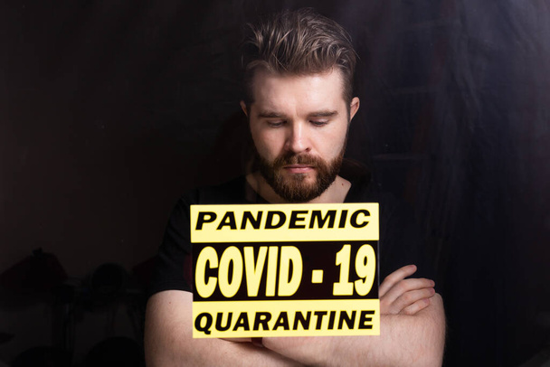 コロナウイルス、隔離、 covid-19およびパンデミックの概念。窓から見るコロナウイルスの悲しい病気の男。家にいて. - 写真・画像