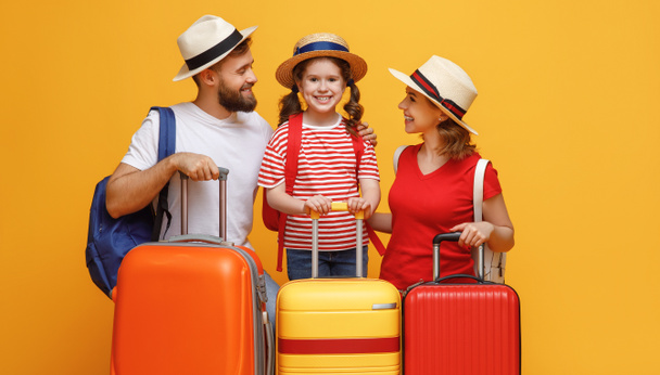 Los padres optimistas y su hija se apoyan en el equipaje y sonríen para la cámara durante las vacaciones de verano contra el backdro amarillo
 - Foto, Imagen