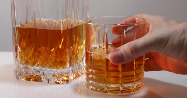 The male hand takes a glass of whiskey or brandy with ice and after a second puts the empty glass in place - Imágenes, Vídeo