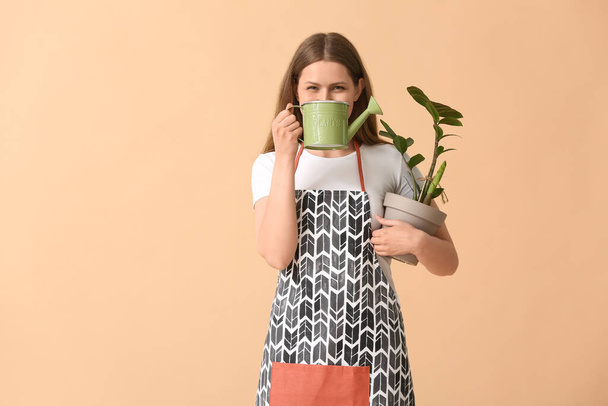 Young woman with watering can and houseplant on color background - Φωτογραφία, εικόνα