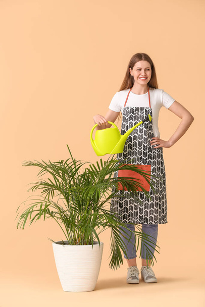 Jeune femme avec arrosoir et plante d'intérieur sur fond de couleur - Photo, image