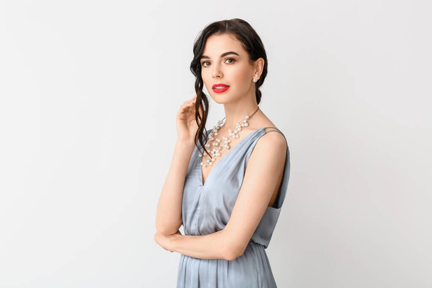Beautiful young woman wearing stylish jewelry on light background - Фото, изображение