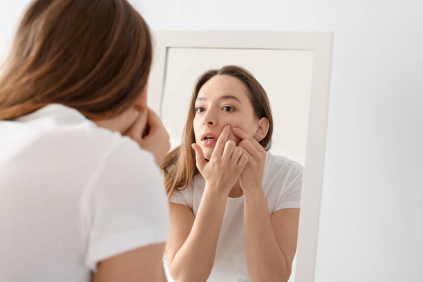 Young woman with acne problem squishing pimples in front of mirror - Photo, Image