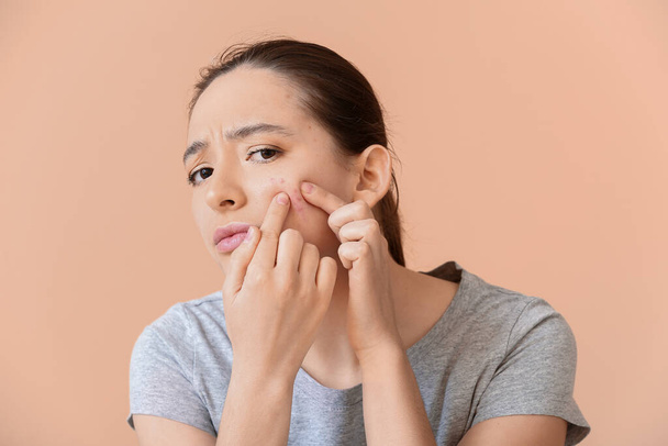 Young woman with acne problem squishing pimples on color background - Foto, afbeelding
