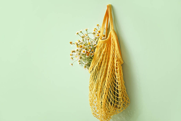 Beautiful chamomiles in bag hanging on color wall - Photo, Image