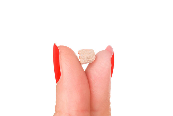 白い背景に隔離された赤い爪を持つ女性の指のエクスタシー錠剤。党薬. - 写真・画像