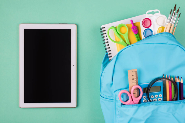 Remote studying concept. Top above overhead view photo of blue backpack filled with colorful stationery and tablet isolated on turquoise background - Foto, afbeelding