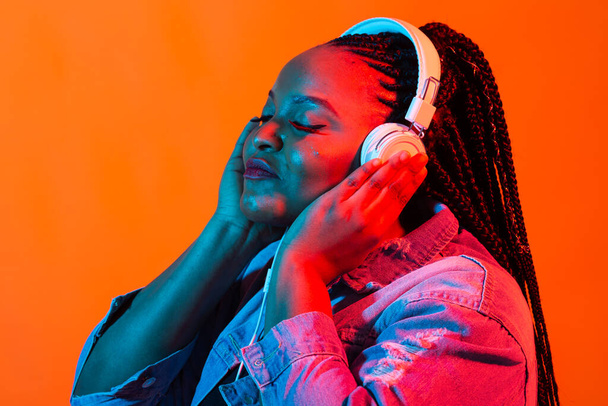 Neon portrait of young black woman listen to music in headphones. - Valokuva, kuva