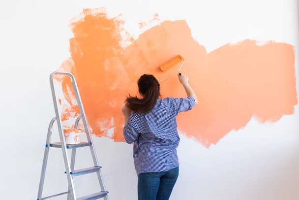 Hermosa mujer pintando la pared en su nuevo apartamento. Concepto de renovación y redecoración. - Foto, imagen