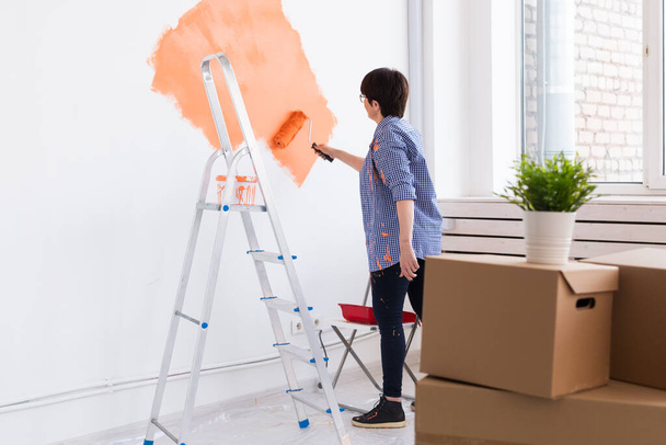 Hermosa mujer de mediana edad pintando la pared en su nuevo apartamento. Concepto de renovación y redecoración. - Foto, imagen